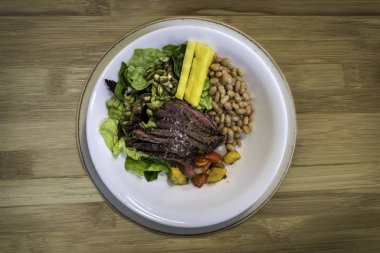 Fasulyeli biftek, ızgara sebze ve ahşap arka planda salata.