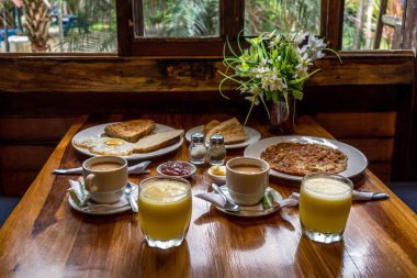 Süt, portakal suyu, tereyağı, reçel, tost, yumurta ve omletten oluşan iki kahvaltı ayrıca tuzluk, biberlik ve vazo da var.