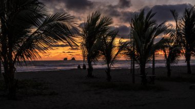 Amazing sunset at the beach. Ocean waves, palm trees, sand and a island can be seen.