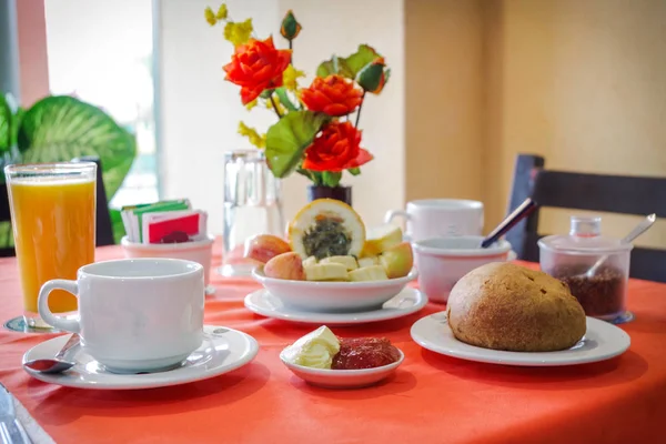 Desayuno en un restaurante compuesto por zumo de naranja, café, mermeladas, pan y algunas frutas tropicales. — Foto de Stock