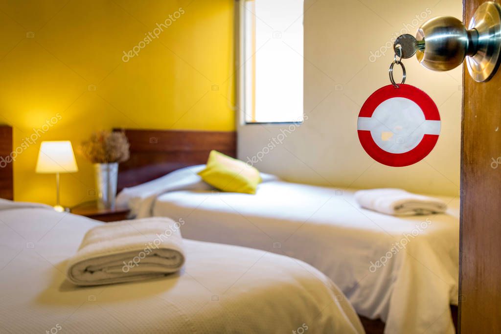 Hotel room with the key ring to complete. In the background you can see two beds, a small vertical window, towels, a vase and a lamp
