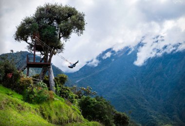 Tourist swinging on the swing of the end of the world (Columpio del fin del mundo) in Banos, Ambato province, Ecuador clipart