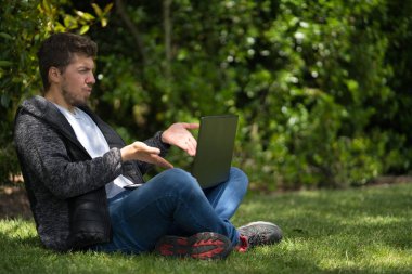 Sarışın adam bilgisayarının ekranına bakıyor ve şikayet ediyormuş gibi ellerini hareket ettiriyor..