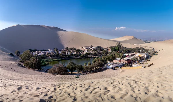 Ica oasis desierto. Laguna en medio de dunas rodeadas de árboles y algunas casas — Foto de Stock