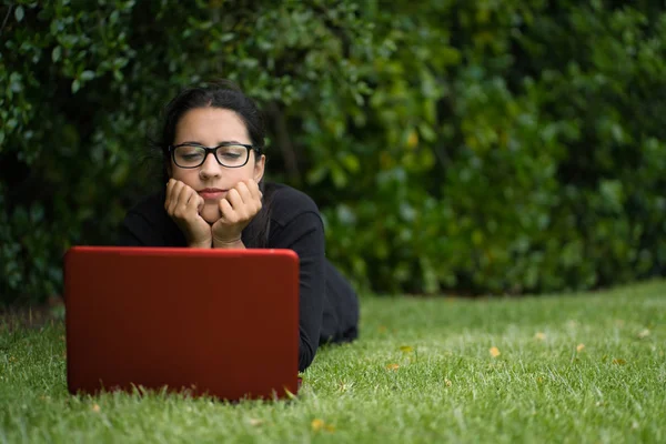 Young woman lying down on the grass of a park while watching the screen of her laptop. Technological concept — Stock Photo, Image