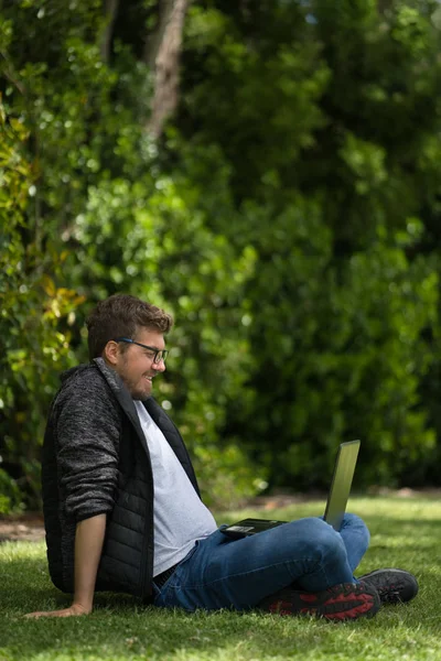 Young man looking at his computer in a park. Natural Environment. Vertical Photography — Stock Photo, Image