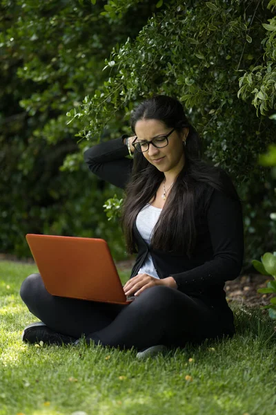 Brunette vrouw zit op het gras met haar laptop. Natuurlijke omgeving. Verticale fotografie — Stockfoto