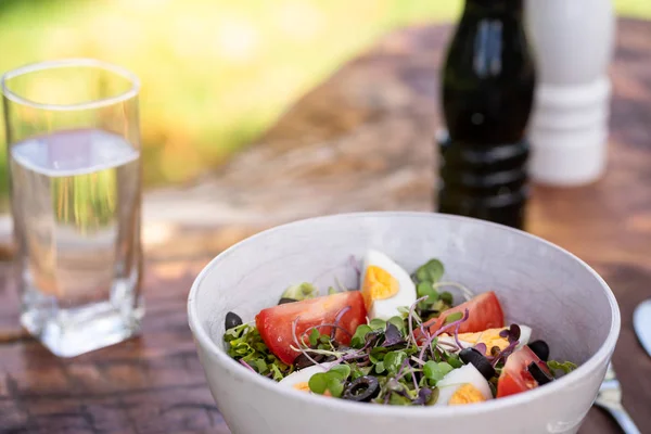 Ensalada de verduras frescas servida en un bol con hojas verdes mixtas, huevos, aceitunas negras y tomate sobre una mesa de madera. Medio ambiente natural — Foto de Stock