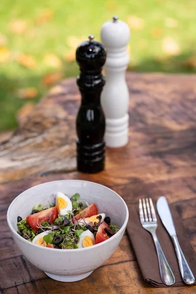 Ensalada de verduras frescas servidas en un tazón sobre una mesa rústica de madera con cubiertos y pimientos y saleros. Medio ambiente natural. Fotografia vertical — Foto de Stock