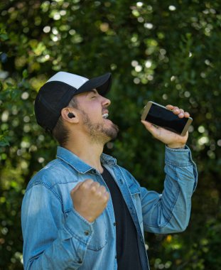 Genç adam akıllı telefon kullanarak şarkı söylüyor ve kablosuz kulaklık takıyor.