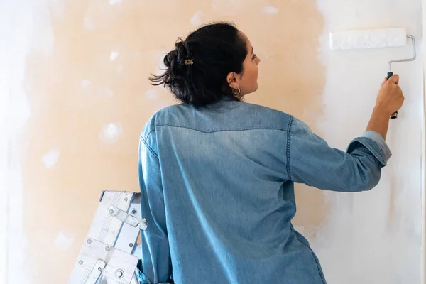 Mulher morena pintando uma parede com um rolo de tinta — Fotografia de Stock