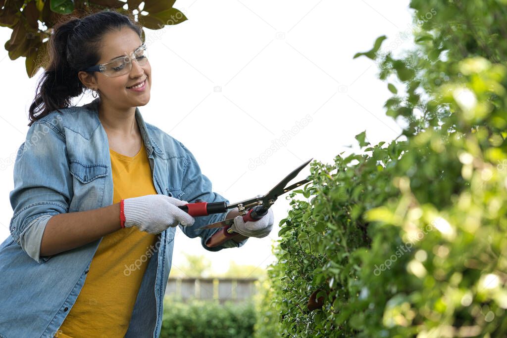 young hispanic woman working on the yard cutting the yard with hedge shear while smiling at home