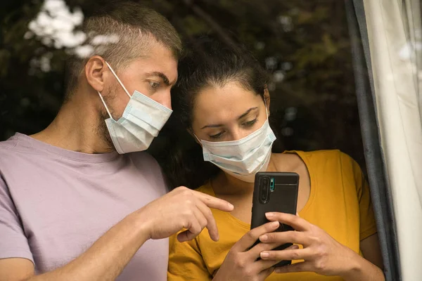 Couple Wearing Face Mask Standing Front Window Watching Smartphone Home — Stock Photo, Image