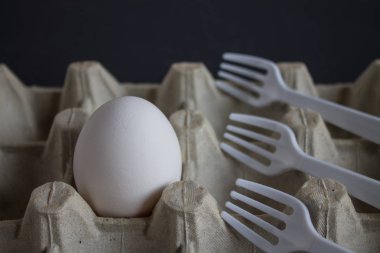 Beyaz yumurta ve plastik çatal karanlık bir arka planda bir hücrede.