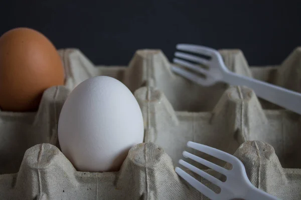 Two eggs and plastic forks in a tray on a dark background