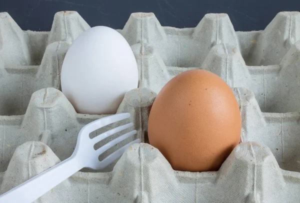 Two eggs and plastic forks in a tray on a dark background
