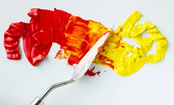Beyaz bir palette kırmızı ve sarı yağlı boya karışımı.