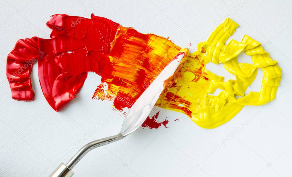Mixing red and yellow oil paints on a white palette close up