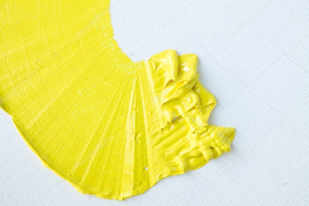 Expressive smear of bright yellow oil paint on a white textured canvas close up