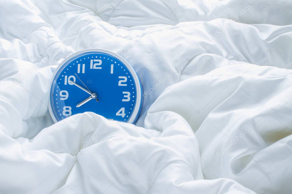 Blue alarm clock on a white blanket with folds