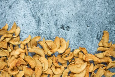 Bir avuç kuru elma, gri desenli bir yüzeye yakın duruyor.