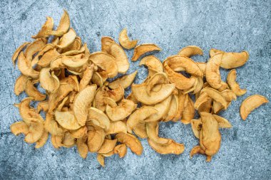 Bir avuç kuru elma, gri desenli bir yüzeye yakın duruyor.