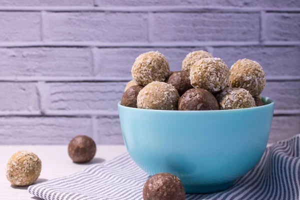 Energy balls of peanut paste and cocoa with oatmeal in a ceramic plate with a kitchen towel on a white wooden table and a brick wall background