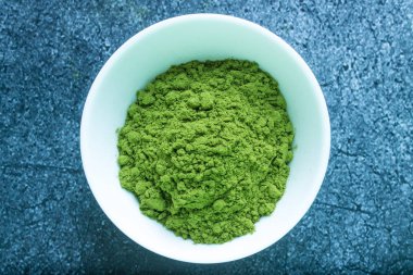 Beyaz porselen bir fincanda kurutulmuş yeşil Japon çayı. Gri desenli arka plana yakın, kopyalamak için alanı var.