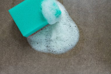 Gri-kahverengi yüzey üzerinde beyaz köpüklü yeşil sünger ve fotokopi alanı. Kavram temizliği