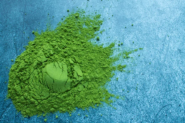 Scattered green powder of traditional Japanese matcha tea in close-up on a grey textural background with copy space