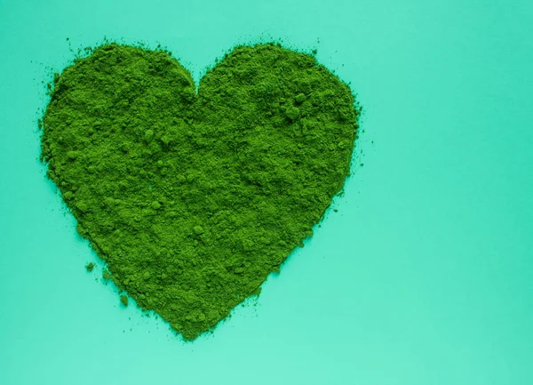Heart of green powdered Japanese matcha tea close-up on a mint-colored background with space to copy