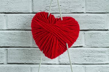 Beyaz ahşap arka planda telleri olan ve kopyalamak için alanı olan kalp şeklinde kırmızı bir iplik yumağı.