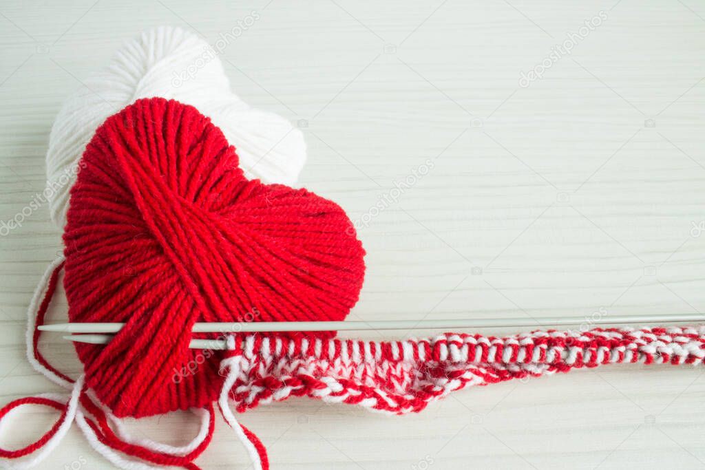 A ball of red yarn in the shape of a heart with spokes on a white wooden background with space for copying