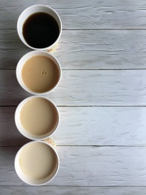 Four paper cups of coffee with milk on a wooden white background close up with space for copying. Flat lay clipart