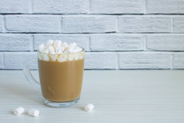 Sütlü kahve bardağı ve ahşap bir masanın üzerinde beyaz şekerlemeler fotokopi alanı olan tuğla bir duvara karşı.