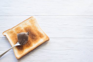 Ekmek üzerine bir kaşık dolusu çikolata ezmesi. Fotokopi alanı olan beyaz bir arka planda yakın plan.