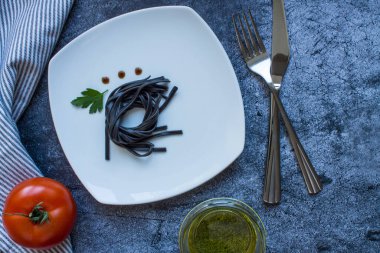 Beyaz kare tabakta mürekkep balığı mürekkebi ve maydanoz yaprağı ve gri desenli arka planda fotokopi alanı olan sos damlaları. Minimalizm
