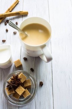 Kahverengi şeker kamışı, tarçın tüpleri ve beyaz ahşap arka planda fotokopi alanı olan yıldız anason kaplı beyaz bardakta sütlü bir fincan kahve. Yemek fotoğrafı..