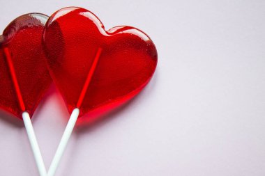 Kırmızı çubuklar üzerinde iki şeffaf lolipop, fotokopi alanı olan açık bir arkaplanda kalp şeklinde.