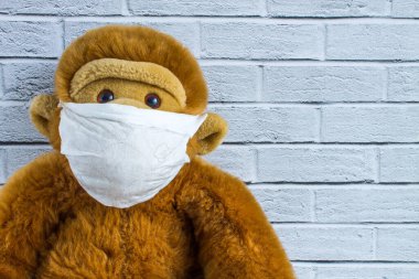 Ev yapımı tıbbi maske takan oyuncak pelüş maymun, duvarda kopyalamak için yeri olan bir tuğla duvar. Kavram - koronavirüsten korunma.