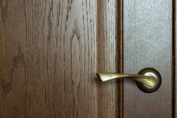 Fragment of a wooden brown textured door with a metal door handle close-up with copy space. Concept: hygiene, coronavirus