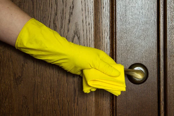 Hand in a yellow rubber glove wiping the door handle close - up with copy space. Concept: the coronavirus.