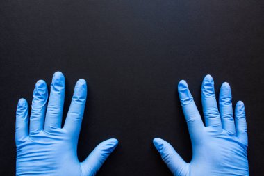 Siyah arka planda, iki eli mavi lastik eldivenli, yakın çekim alanı olan bir yer. Konsept: çerçeve tıbbi metin içindir.