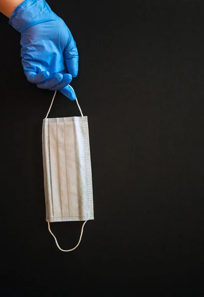 Hand in a transparent glove with a disposable medical mask on a black background. Concept: means of protection during coronavirus quarantine.