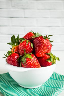 Beyaz bir fincanda parlak kırmızı çilek. Fotokopi alanı olan beyaz arka planda yeşil tekstil.