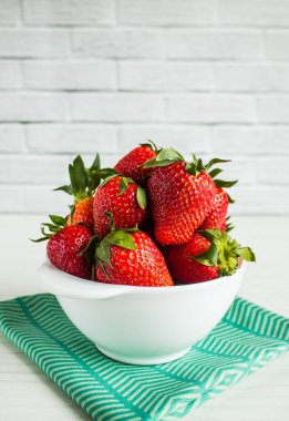 Beyaz bir fincanda parlak kırmızı çilek. Fotokopi alanı olan beyaz arka planda yeşil tekstil.