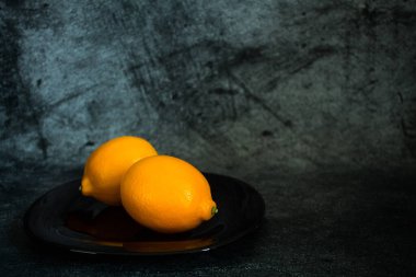 Gri desenli arka planda siyah bir tabakta iki parlak olgun limon.