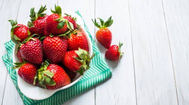 Beyaz bir fincanda parlak kırmızı çilek yakın plan beyaz ahşap zemin üzerinde yeşil tekstil uzay manzaralı