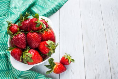 Beyaz bir fincanda parlak kırmızı çilek yakın plan beyaz ahşap zemin üzerinde yeşil tekstil uzay manzaralı