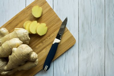 Ahşap mutfak tahtasının üzerinde dilimlenmiş parçalarla taze zencefil kökü ve siyah bir arka plana yakın bir bıçak.